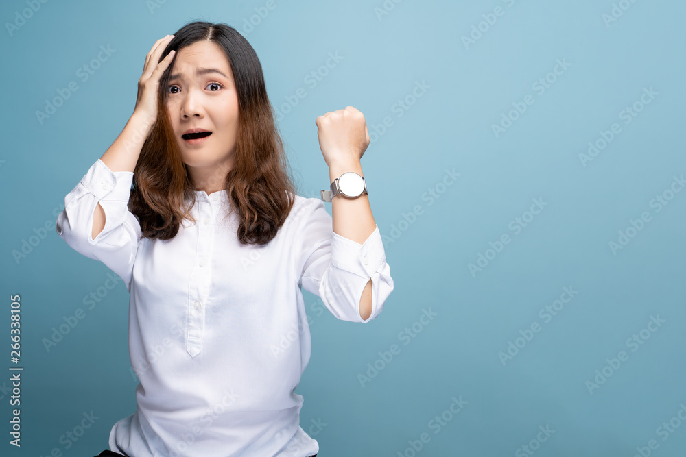Shocked woman holding hand with wrist watch isolated on a blue background Shocked woman holding hand with wrist watch isolated on a blue background
