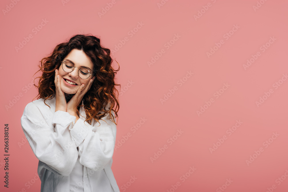 happy curly woman in glasses smiling while touching face on pink happy curly woman in glasses smiling while touching face on pink