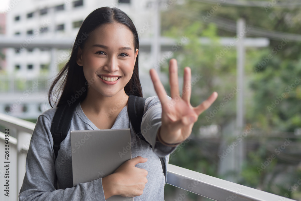 portrait of happy smiling asian woman college student pointing up 4 fingers, four points pose; winning, forth concept in city campus environment portrait of happy smiling asian woman college student pointing up 4 fingers, four points pose; winning, forth concept in city campus environment