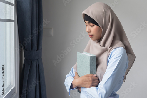 young adult asian muslim woman with the Quran, islamic holy book; concept of Ramadan, Eid al Fitr, meditation, islamic praying, islam religion education, muslim religious activities