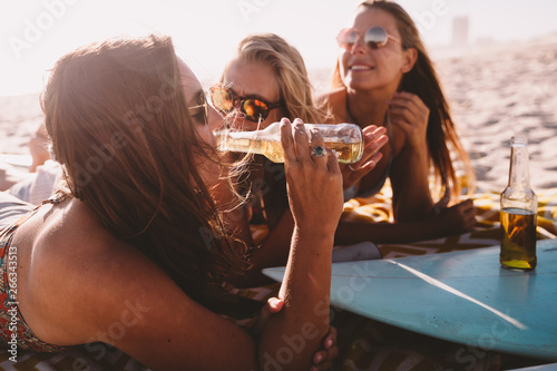 group of friends drinking beer on beach in summer