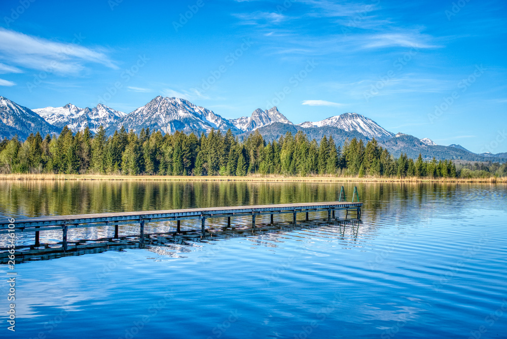Alpensee zum Schwimmen mit Steg mit Bergen im Frühling
