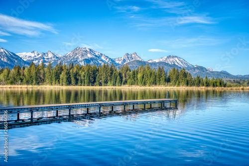 Alpensee zum Schwimmen mit Steg mit Bergen im Frühling