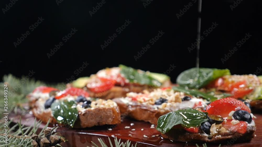Food serving concept. Vegetarian concept. Variety of fresh homemade sandwiches on wooden background. Isolated on black. Olive oil is poured down in slow motion. hd