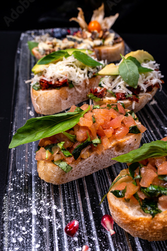 Tasty savory tomato Italian appetizers, or bruschetta, on slices of toasted baguette garnished with basil and avocado.
