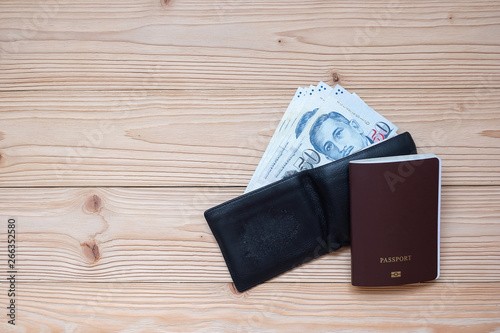 Money banknote in black wallet with Passport on wooden table, Top view and copy space. Time to Travel in Singapore concept