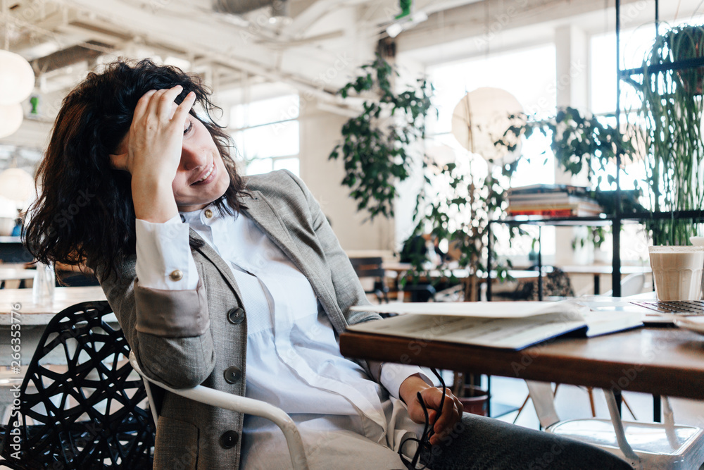 Fototapeta premium Tired happy business woman wearing suit sitting and resting in city cafe with notepad