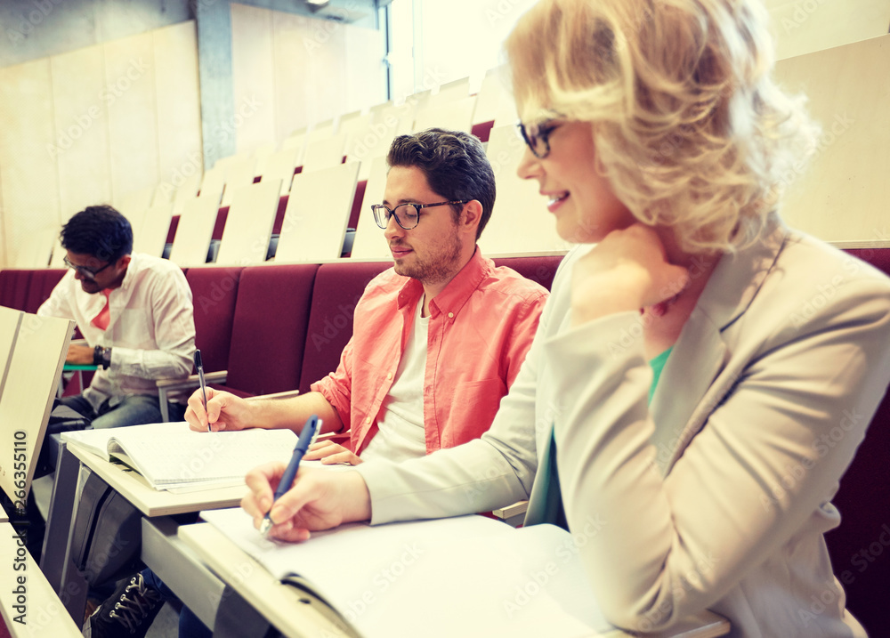 education, high school, university, learning and people concept - group of international students with notebooks writing at lecture hall education, high school, university, learning and people concept - group of international students with notebooks writing at lecture hall