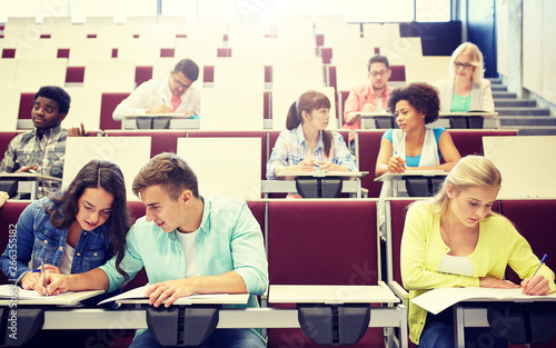 education, high school, university, learning and people concept - group of international students with notebooks writing at lecture hall