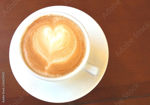 White cup with Italian cappuccino coffee with pattern in the shape of beautiful heart close up on brown wooden background