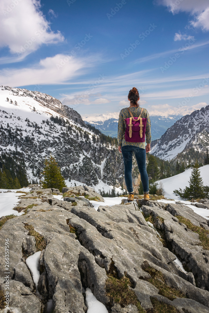 Girl with purple backpack standing on mountain peak looking to beautiful view over the european Alps in Austria.