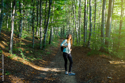 Young woman taking a walk in the forest  carrying a backpack in the forest on sunset light in the autumn season.