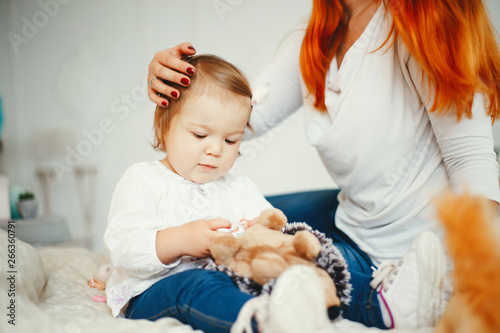 Beatuful ginger mother playing with daughter. Little girl sitting on a bed at home. A young mother clinging to a daughter of hair
