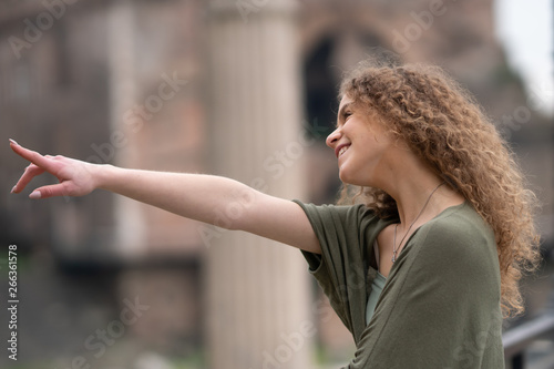 Young woman as tourist in Rome, Italy, looking and pointing at touristic site
