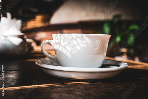 White tea cup with open shadow on rustic wooden table. Cozy tea time atmosphere.