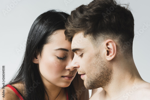 beautiful asian woman with handsome pensive boyfriend standing face to face with closed eyes on grey
