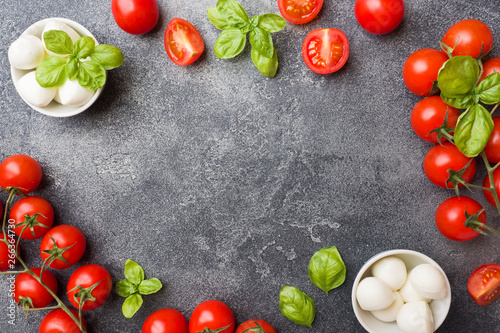 The ingredients for a Caprese salad. Basil, mozzarella balls and tomatoes on a dark concrete background with copy space.