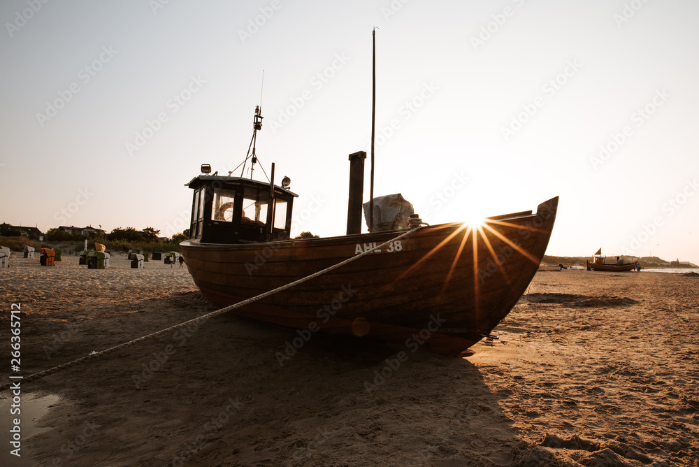 Fischerboot bei Sonnenuntergang am Strand im Sommer im Gegenlicht Fischerboot bei Sonnenuntergang am Strand im Sommer im Gegenlicht