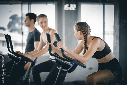 Group of people biking in the gym  exercising legs doing cardio workout cycling bikes. Couple in a spinning class wearing sportswear. Fitness  Healthy  Sport  Lifestyle concept.