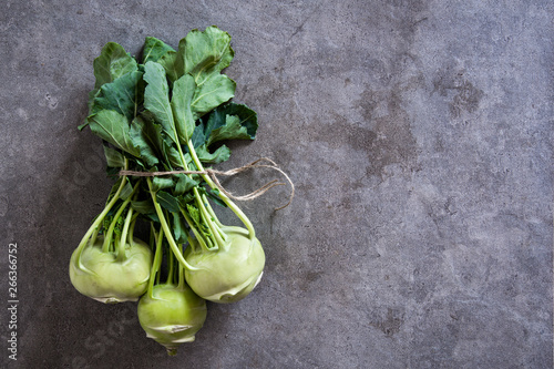 Bundle of fresh kohlrabi stems with leafs over grey concrete background photo