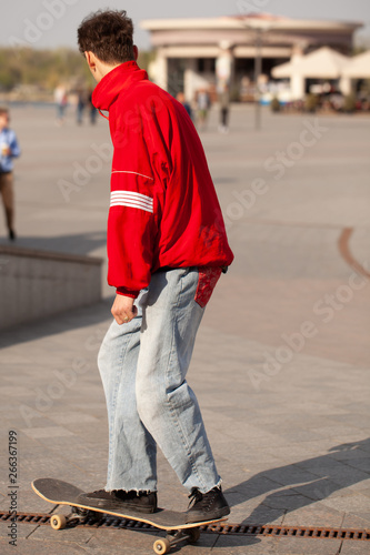 Young guys in stylish clothes ride a skateboard in the park.