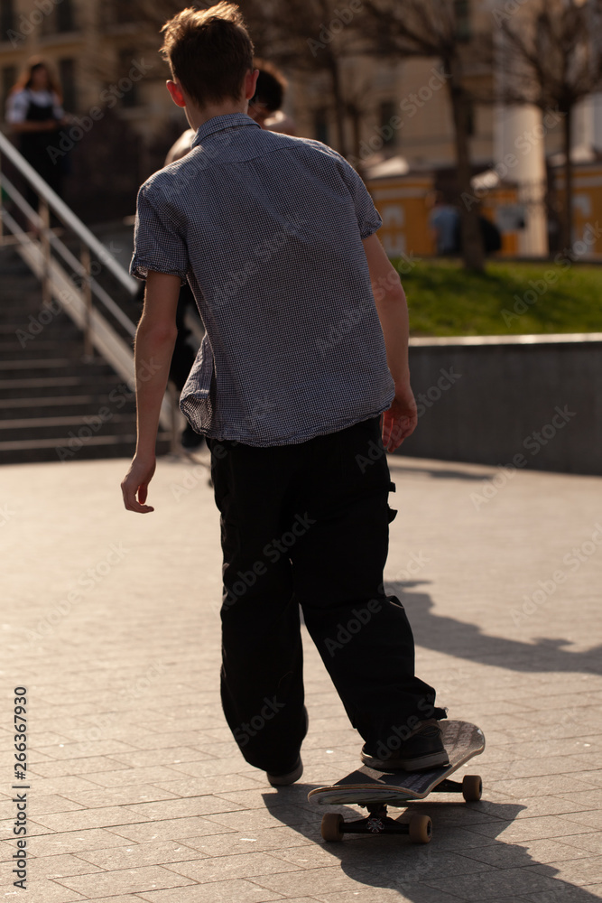Obraz premium Young guys in stylish clothes ride a skateboard in the park.