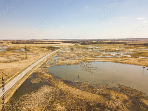 Aerial view of a marshland near a highway with an asphalt road during a spring flood  which floods and blurs the road under a clear blue sky without clouds. Natural disasters of the environment.