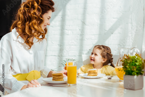 cute child looking at happy mother while having breakfast together