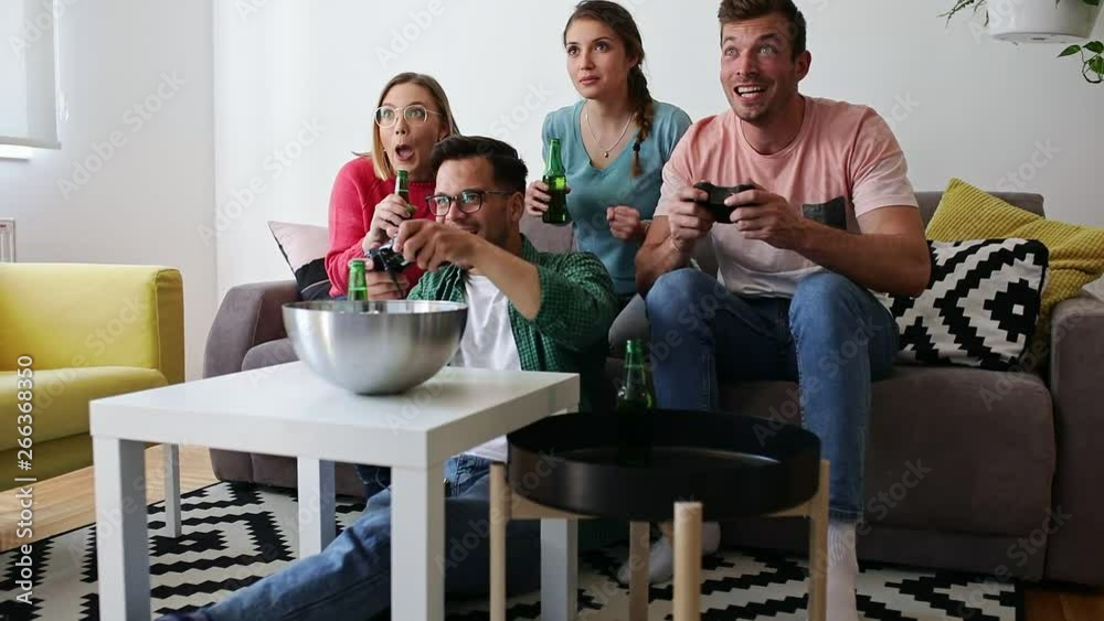 Group of friends sitting on sofa in living room and playing video games at home. Group of friends sitting on sofa in living room and playing video games at home.