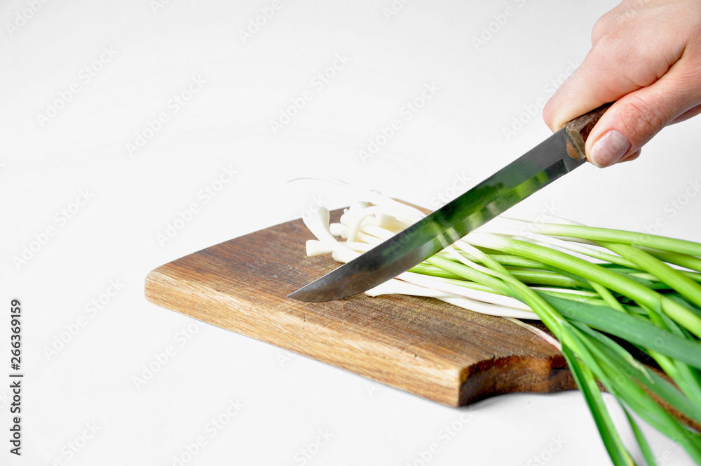 young fresh green garlic on a cutting board with a knife. Hand holds knife on white background. young fresh green garlic on a cutting board with a knife. Hand holds knife on white background.