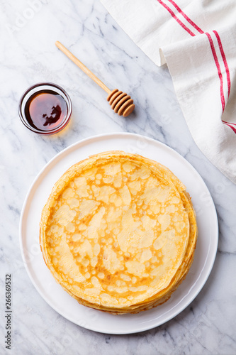 Crepes, blini, thin pancakes with honey on a white plate. Marble background. Top view.