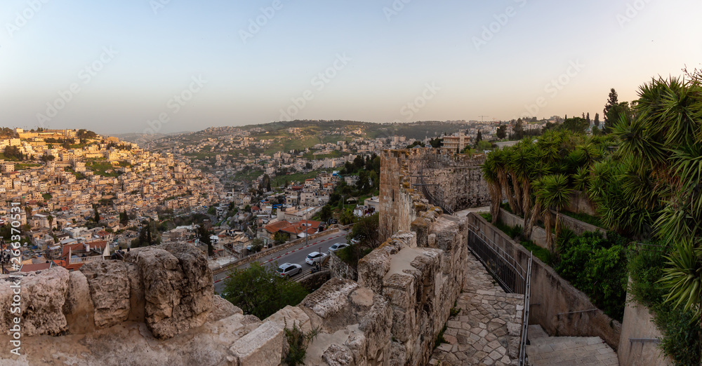 Beautiful panoramic view of the Walls of Jerusalem surrounding the Old City with the cityscape in the background during a sunny sunset. Taken near the Jerusalem, Israel.