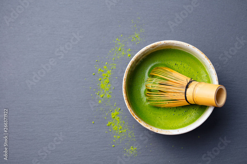 Matcha green tea cooking process in a bowl with bamboo whisk. Black slate background. Top view. Copy space.