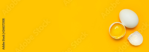 Fotografia White chicken eggs and one broken egg with yolk on yellow background top view flat lay copy space