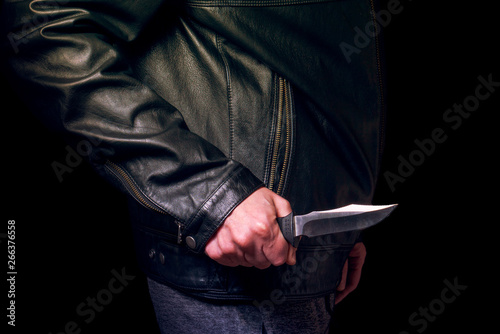 A man in a black leather jacket with a knife in his hand, no face