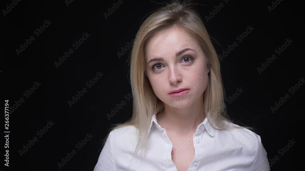 Pretty young blonde businesswoman with big brown eyes in white shirt watches attentively on black background. Pretty young blonde businesswoman with big brown eyes in white shirt watches attentively on black background.