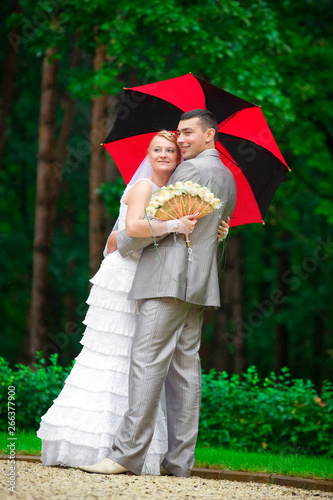Wedding beautiful couple walking in green summer park together with umbrella under the rain. Loving romantic couple  bride and groom