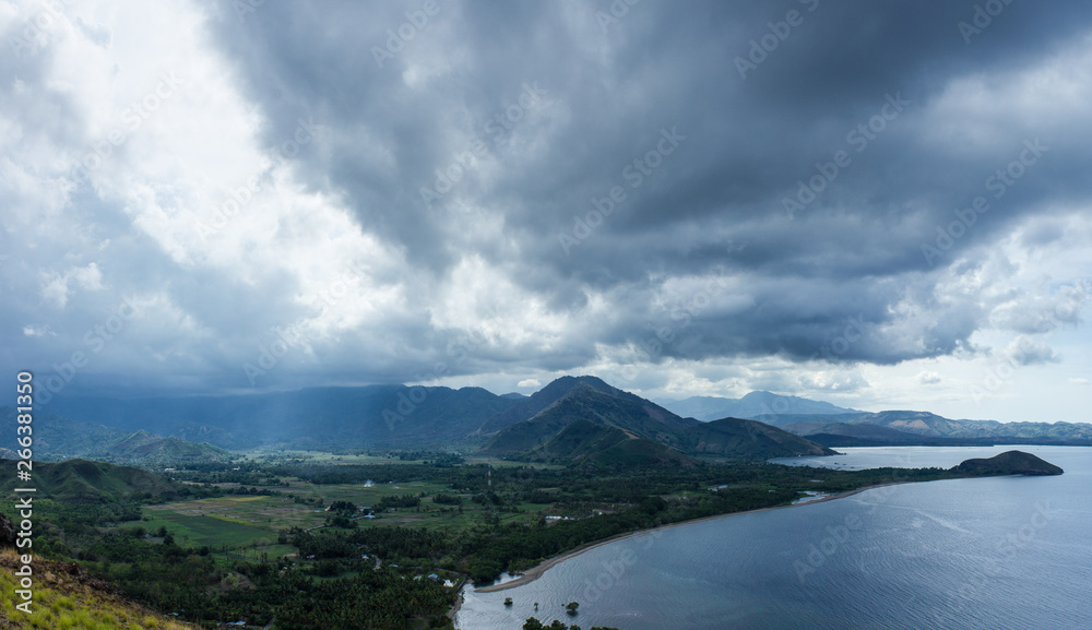 Scenic landscape Picture of land and sea on the deep village in Flores islands during the cloudy and windy day with sun rays goes through the clouds. Beautiful Indonesian nature