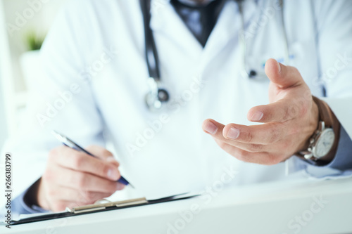 Male doctor making welcome gesture  politely inviting patient to sit down in medical office.
