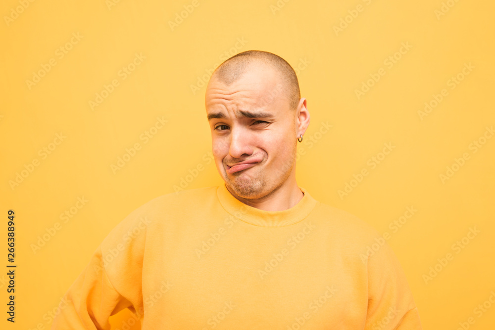 Funny young man in a yellow sweatshirt makes a funny face and looks at the camera on a yellow background. Bald man with a bristle makes a crazy face,isolated on a yellow background Funny young man in a yellow sweatshirt makes a funny face and looks at the camera on a yellow background. Bald man with a bristle makes a crazy face,isolated on a yellow background