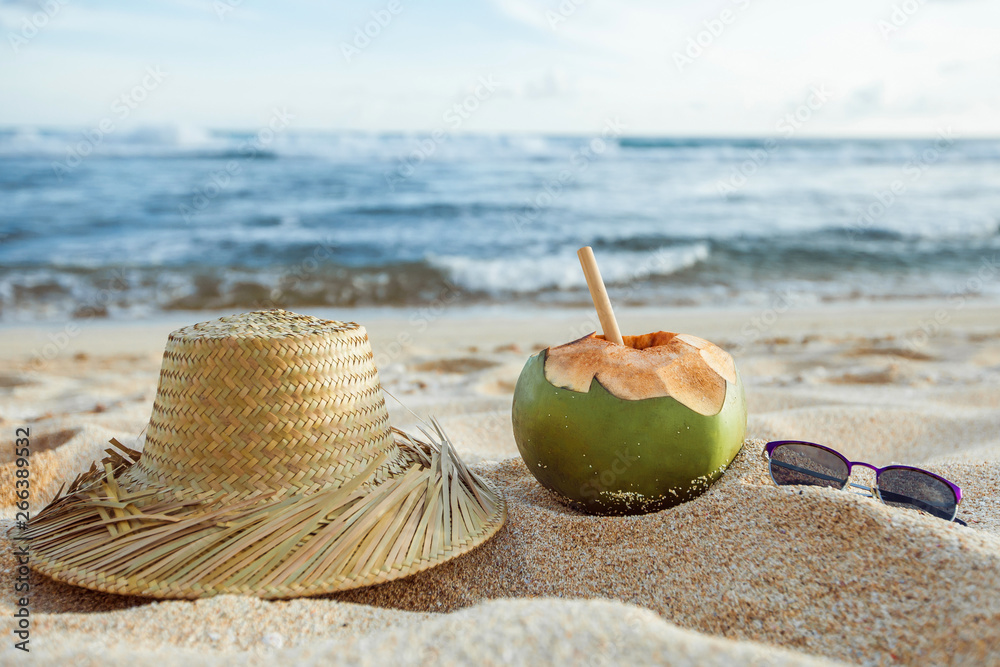 A young coconut with a solvin hat and sunglasses lies on the beach on the sand. Summer background. Summer holiday concept