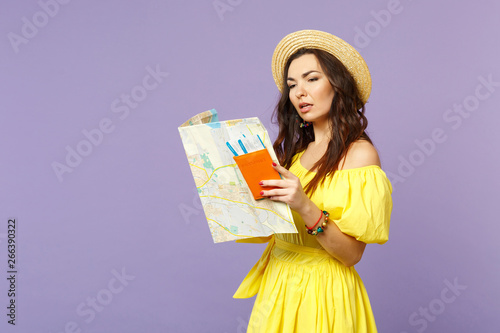 ?urious young woman in yellow dress, summer hat hold city map, passport boarding pass ticket isolated on pastel violet wall background. People sincere emotions, lifestyle concept. Mock up copy space. photo