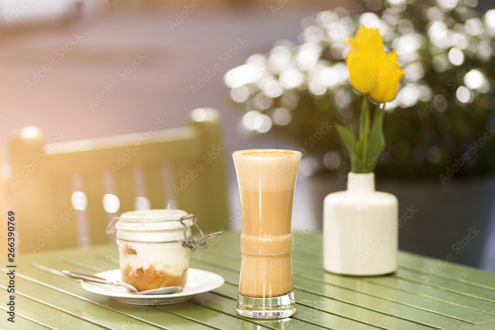 Latte coffee with cake in jar on the table in the street, terrace, outdoor cafe, sunset, outdoors . Free space for text