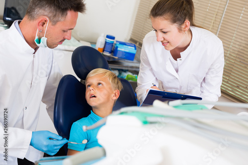Dentist guy is diagnosing the child while assistant is writing down patient s complaint
