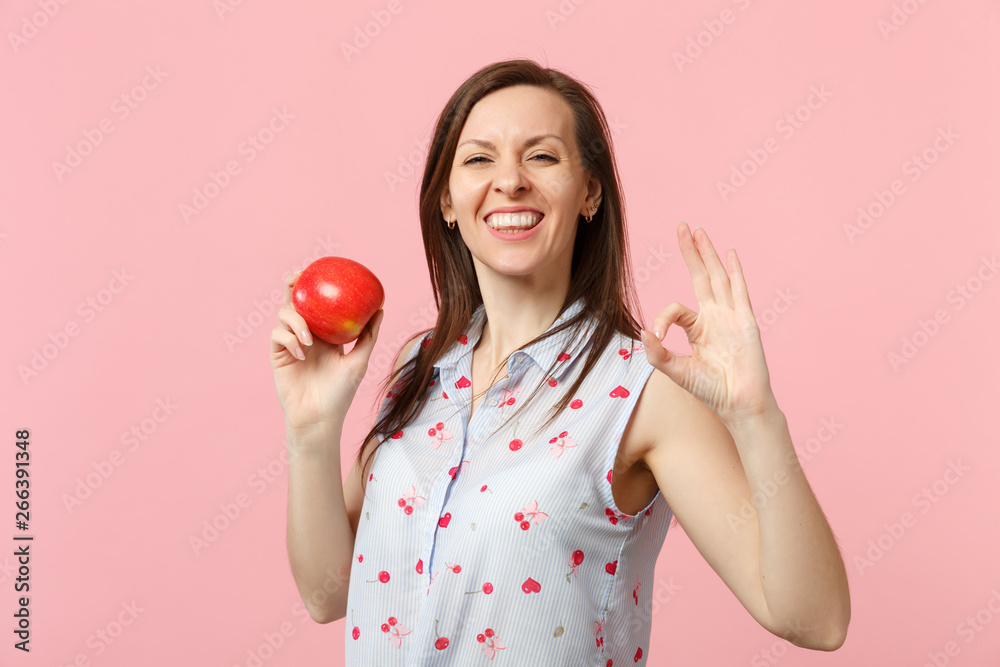Smiling young woman in summer clothes showing OK gesture holding fresh ripe red apple fruit isolated on pink pastel wall background. People vivid lifestyle, relax vacation concept. Mock up copy space. Smiling young woman in summer clothes showing OK gesture holding fresh ripe red apple fruit isolated on pink pastel wall background. People vivid lifestyle, relax vacation concept. Mock up copy space.