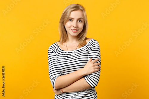 Portrait of beautiful young woman in striped clothes looking camera holding hands crossed isolated on yellow orange background in studio. People sincere emotions lifestyle concept. Mock up copy space.