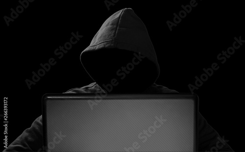 hacker with glowing mask behind notebook laptop in front of isolated black background internet cyber hack attack concept photo