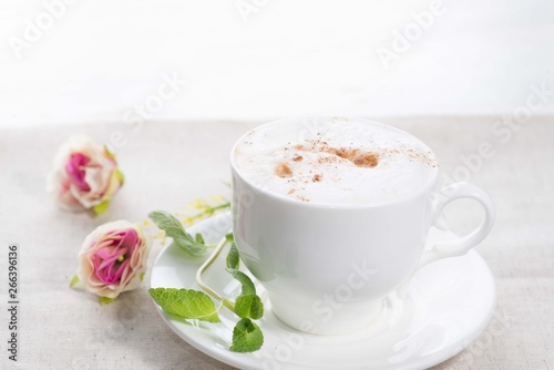 white cup of coffee on a background of scattered flower buds on a white background