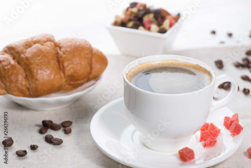 cup of coffee and a croissant on a served table with flower buds