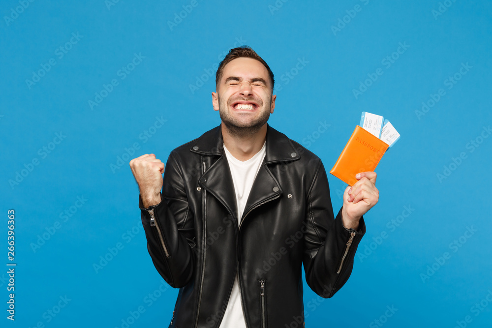 Young happy unshaven man in black jacket white t-shirt hold in hand passport tickets isolated on blue wall background. Passenger traveling abroad getaway. Air flight journey concept Mock up copy space Young happy unshaven man in black jacket white t-shirt hold in hand passport tickets isolated on blue wall background. Passenger traveling abroad getaway. Air flight journey concept Mock up copy space